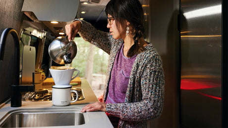 Start your day right! A woman makes fresh pour-over coffee in a compact RV rental kitchen.