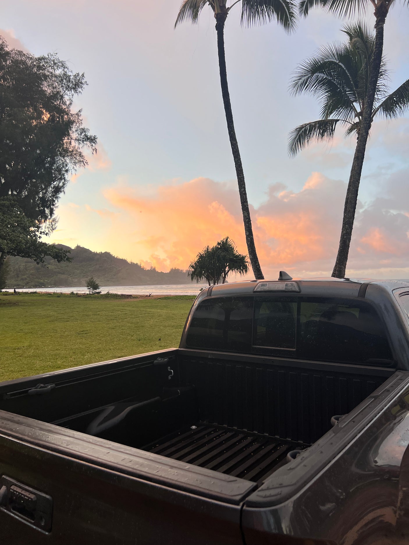Dark pickup truck overlooks tranquil beach & sunset sky with palm trees. Plan your RV rental journey to similar serene spots!