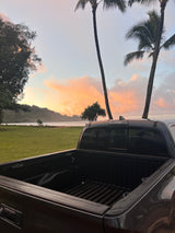 Dark pickup truck overlooks tranquil beach & sunset sky with palm trees. Plan your RV rental journey to similar serene spots!