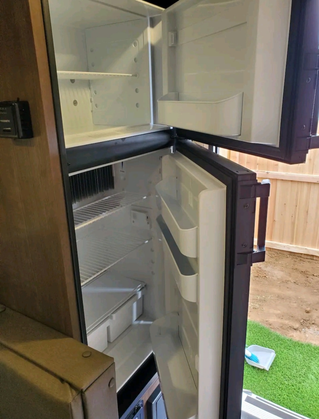 Clean, empty two-door refrigerator/freezer in an RV rental. Ideal for travel food storage, with interior shelves and door bins. — photo 4