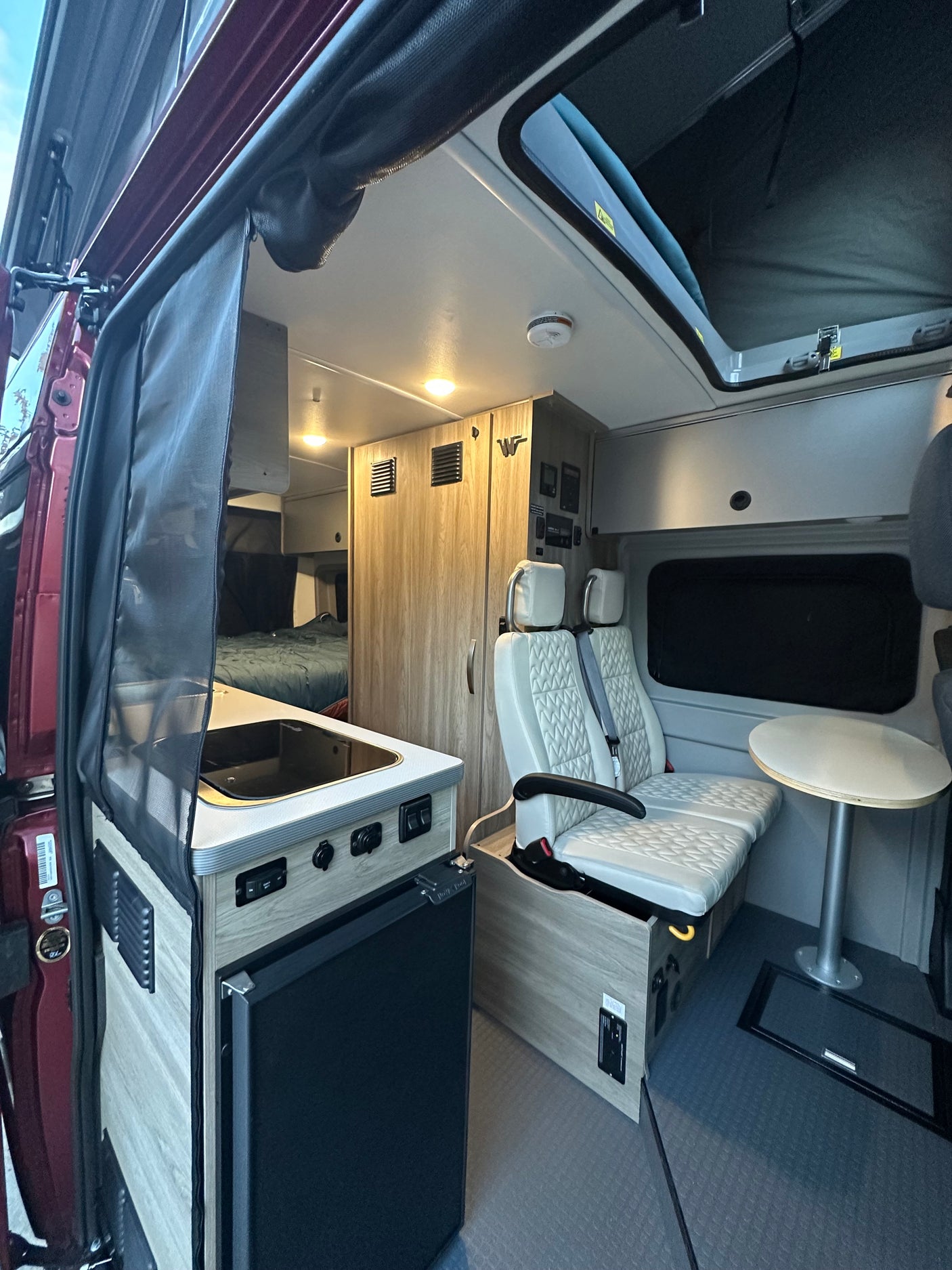 Inside a modern RV rental, featuring a compact kitchen, comfortable seating, rear bed, and versatile pop-top.
