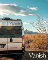 Rear view of a silver Vanish RV rental campervan parked in a desert landscape with mountains and blue sky.