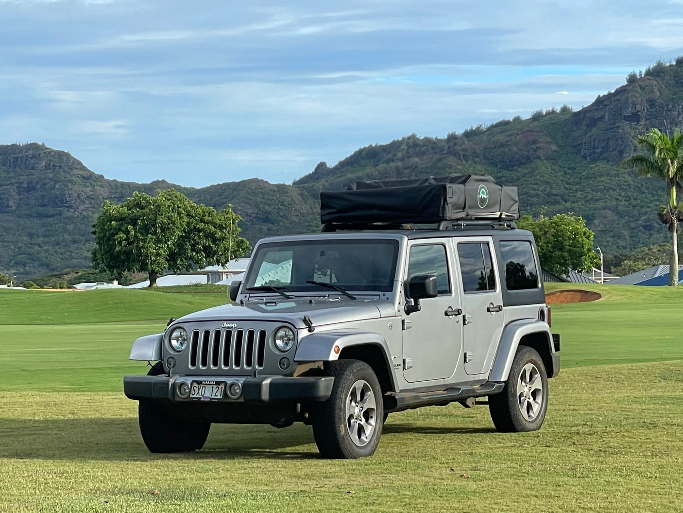 Silver Jeep Wrangler with rooftop tent, ideal for an RV rental adventure amidst Kauai's mountains.