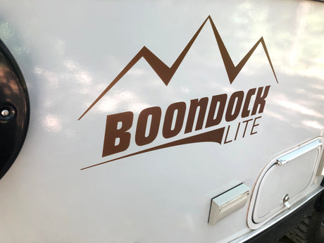 Side of a white RV featuring a brown "BOONDOCK LITE" mountain decal, ideal for an RV rental adventure.
