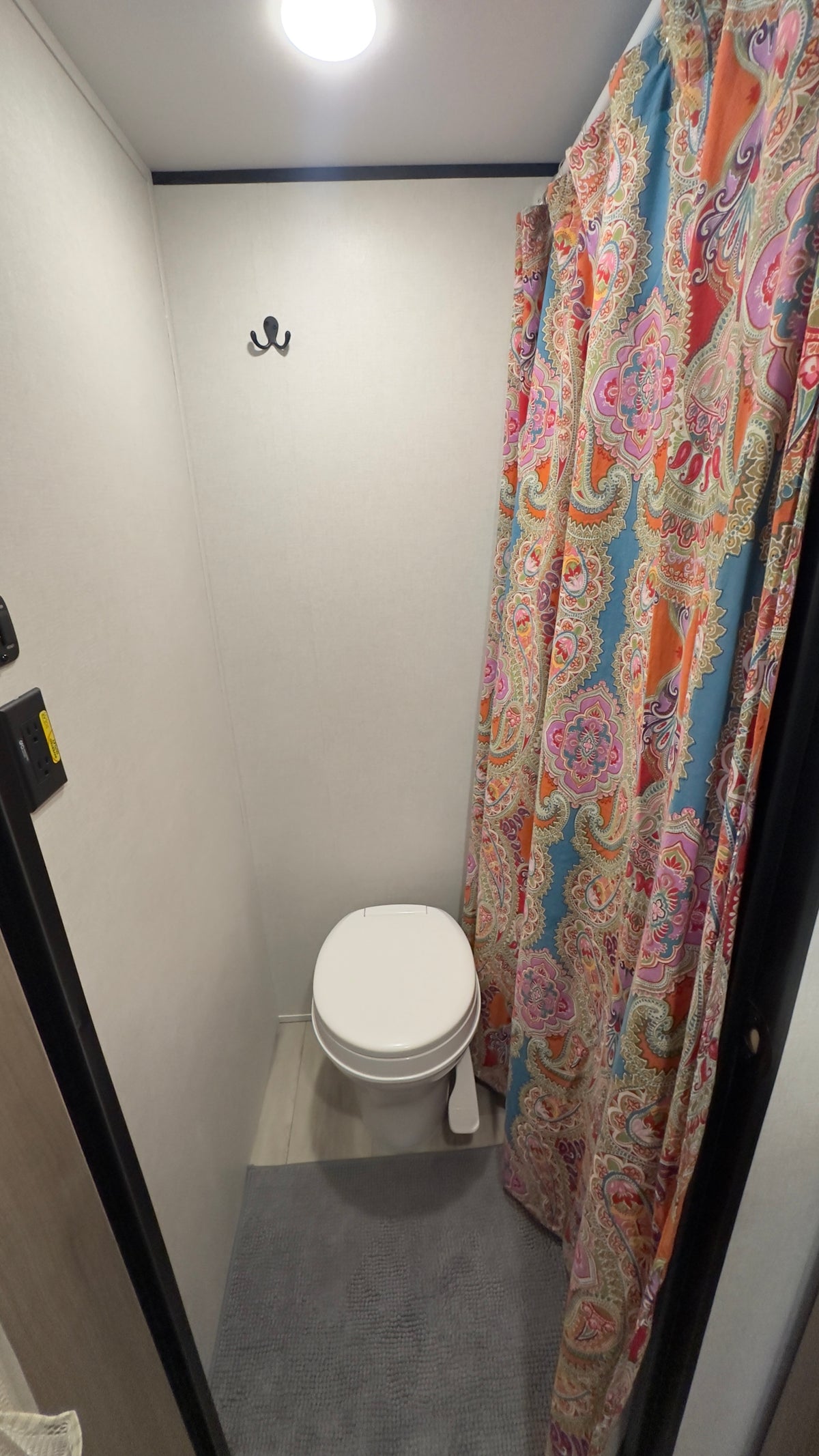 Inside an RV rental, a compact bathroom with a white toilet, vibrant paisley shower curtain, ceiling light, and wall hooks. — photo 7