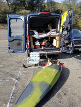 Blue rv rental van prepped for adventure: bed, gear, kayak, and a smiling dog. Ready for a great outdoor escape.