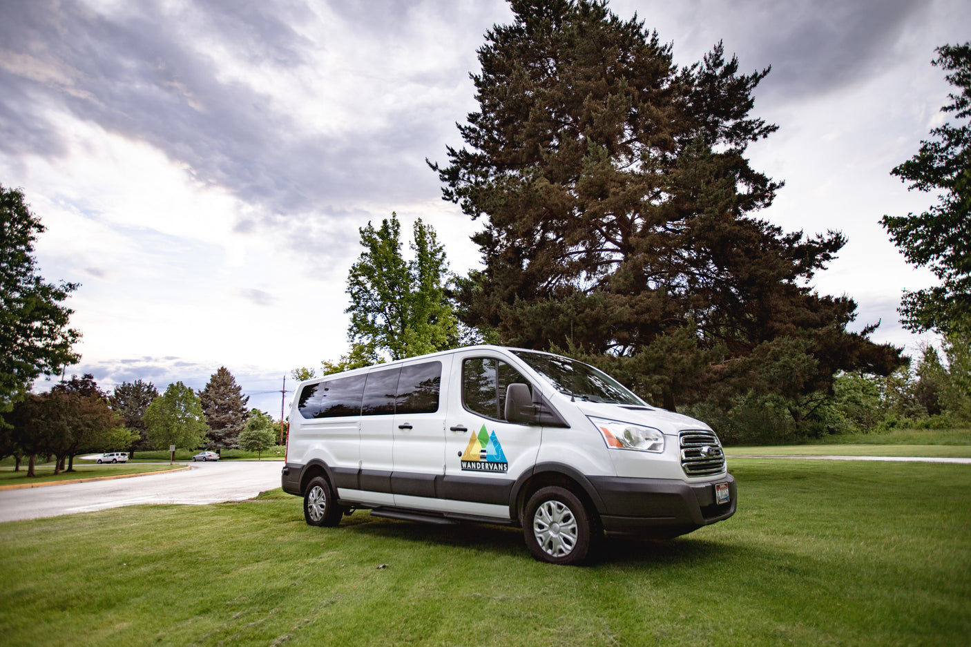 White Wander Vans RV rental van parked on green grass with tall trees under a cloudy sky, ready for adventure.