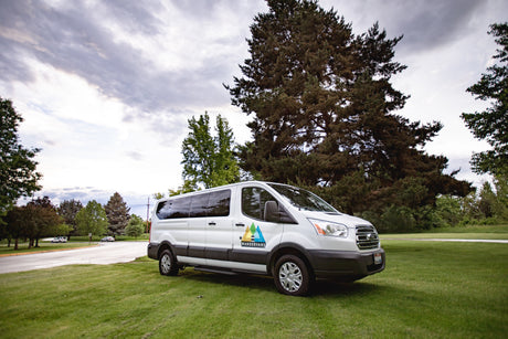 White Wander Vans RV rental van parked on green grass with tall trees under a cloudy sky, ready for adventure.