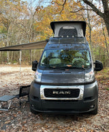An RV rental camper van with pop-top and awning, parked at a fall campsite amidst colorful autumn leaves.