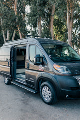 Spacious dark grey camper van with open side door, perfect for your next RV rental adventure among trees.