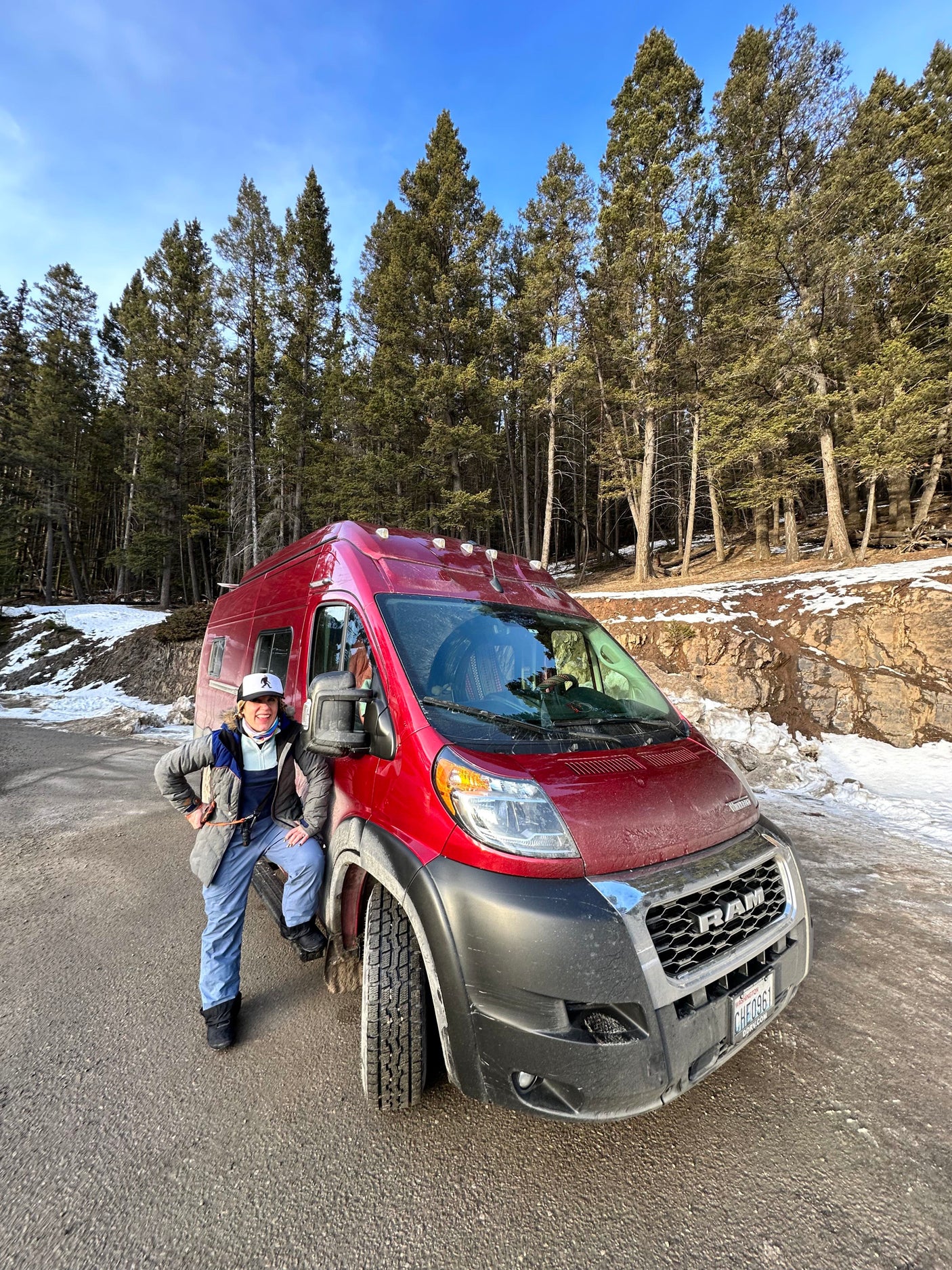 Woman enjoying her **rv rental** adventure, posing by a red camper van in a snowy forest.