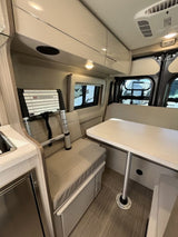 View inside a modern rv rental showing the dinette, compact kitchen, and overhead storage.