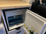 This RV rental features a well-stocked mini-fridge with drinks, a small freezer, and a wooden counter, ready for your travels.