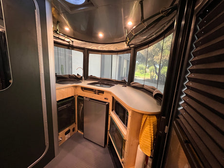 Compact RV rental kitchen interior with sink, fridge, microwave, and scenic window views. Functional camper design.