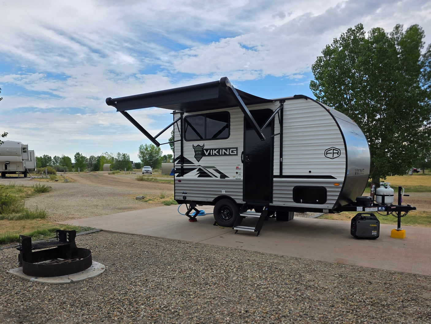 An RV rental with an extended awning is parked on a concrete pad at a campsite