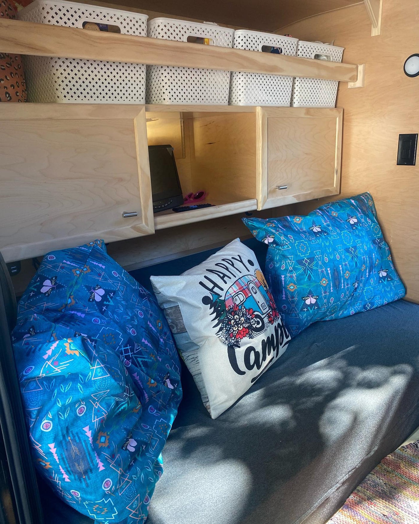 Cozy rv rental interior featuring wooden cabinetry, open shelving with white baskets, and pillows on a dark bed. — photo 2