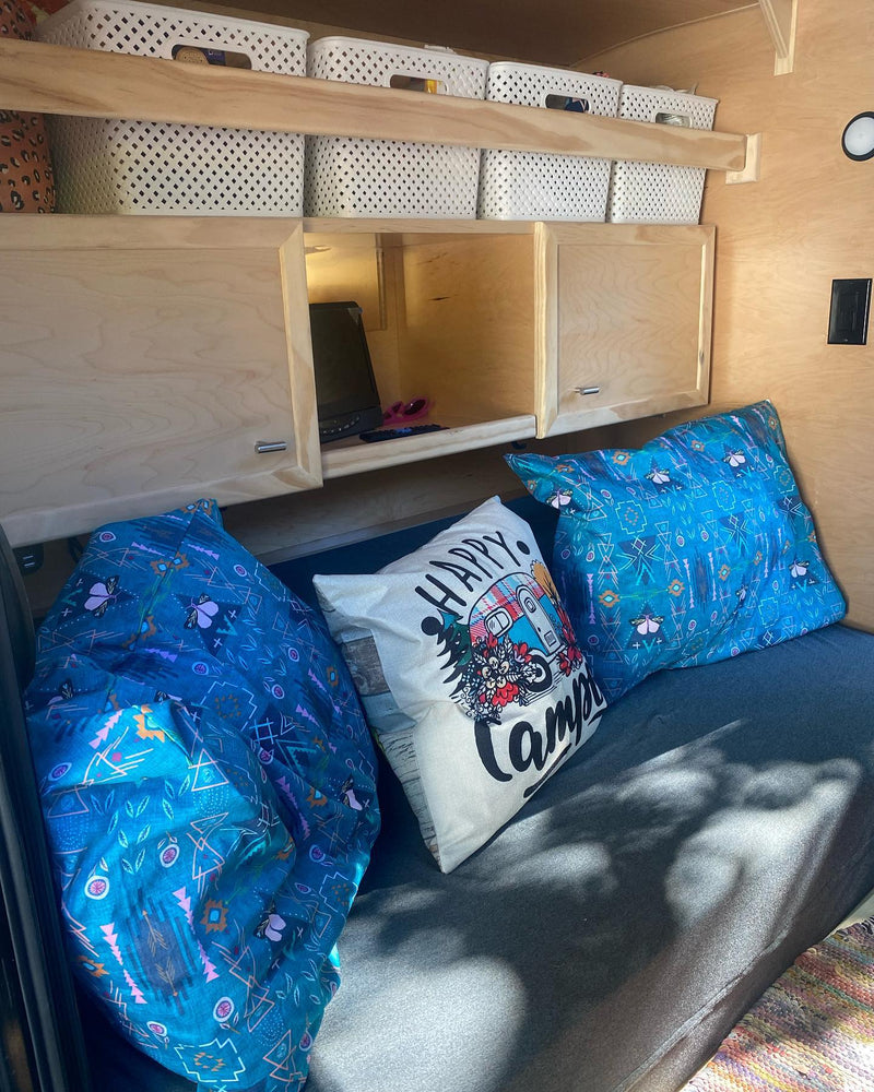 Cozy rv rental interior featuring wooden cabinetry, open shelving with white baskets, and pillows on a dark bed. — photo 2