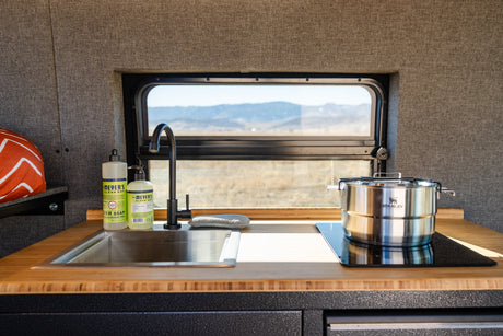 RV rental kitchen: a sleek sink, induction cooktop, Stanley pot, and scenic views, ideal for mobile living.