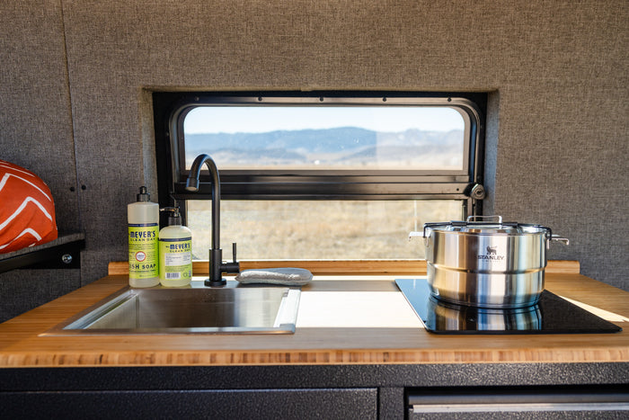 RV rental kitchen: a sleek sink, induction cooktop, Stanley pot, and scenic views, ideal for mobile living.
