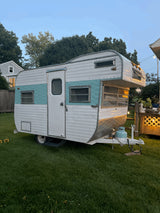 A vintage teal and white travel trailer on grass, seen at dusk. Perfect for an RV rental or camping adventure.