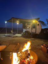 Nighttime rv rental camping scene with a lit teardrop RV under an awning and a bright campfire.
