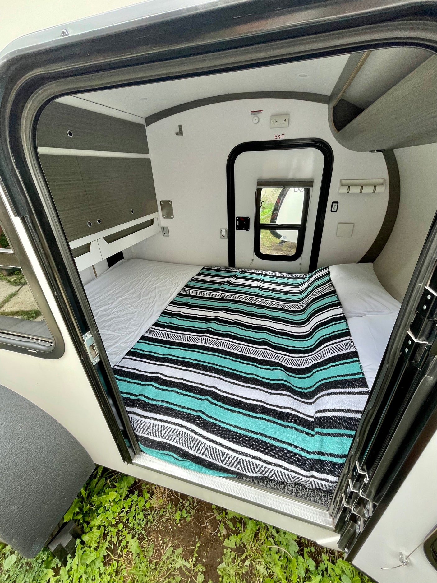 View into a modern RV rental sleeping area with a striped blanket, white sheets, and built-in storage cabinets.