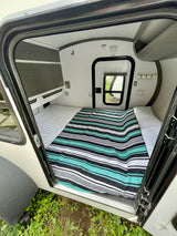 View into a modern RV rental sleeping area with a striped blanket, white sheets, and built-in storage cabinets.