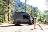 Experience nature with an RV rental! A woman and girl exit their camper van in a beautiful mountain park setting.