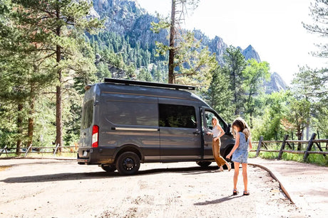 Experience nature with an RV rental! A woman and girl exit their camper van in a beautiful mountain park setting.