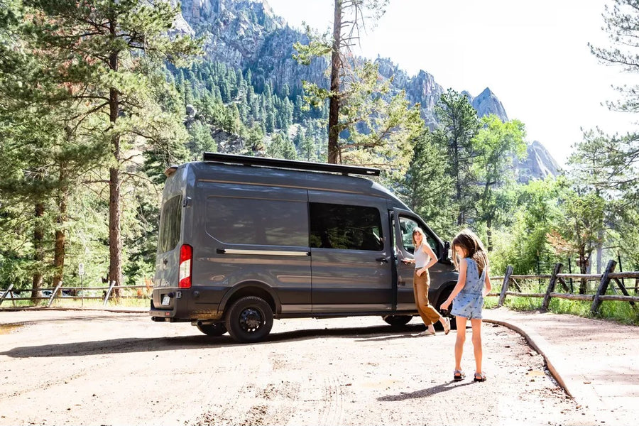 Experience nature with an RV rental! A woman and girl exit their camper van in a beautiful mountain park setting.