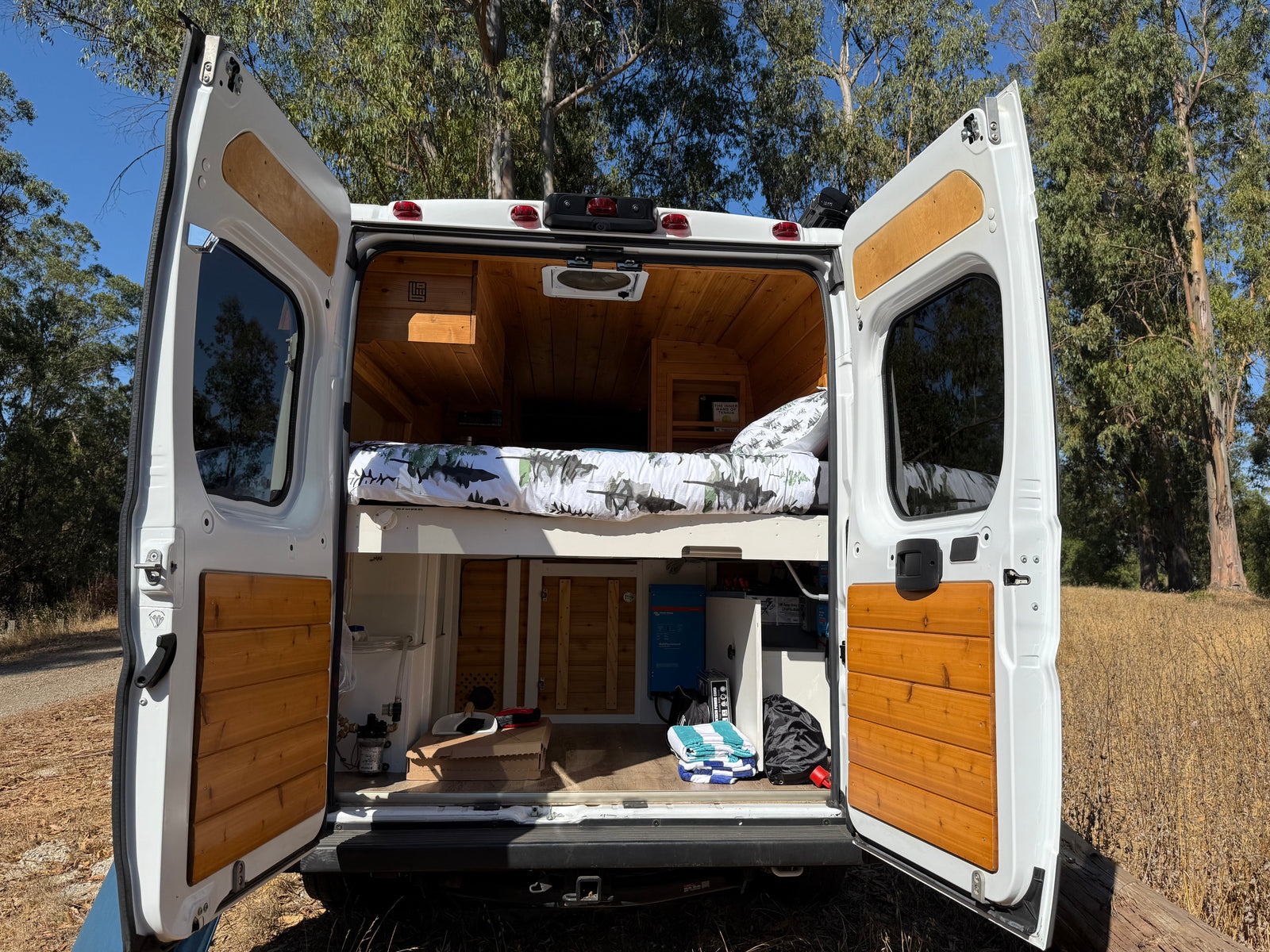 This RV rental showcases its custom-built interior, with open rear doors revealing a cozy bed, wood paneling, and power system.
