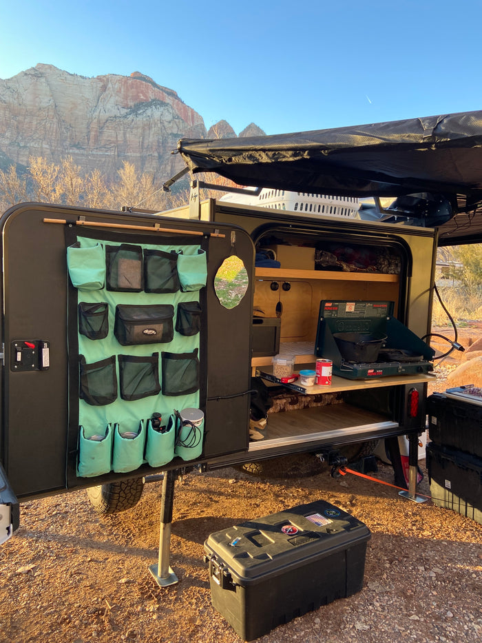 An RV rental camper's open outdoor kitchen with a stove and organizer, set against majestic mountains at sunrise.