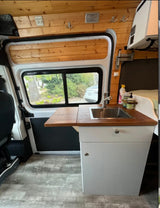 Bright **RV rental** interior boasts a compact kitchen with a sink, wood counters, and cozy wood-paneled walls. Ready for adventure!