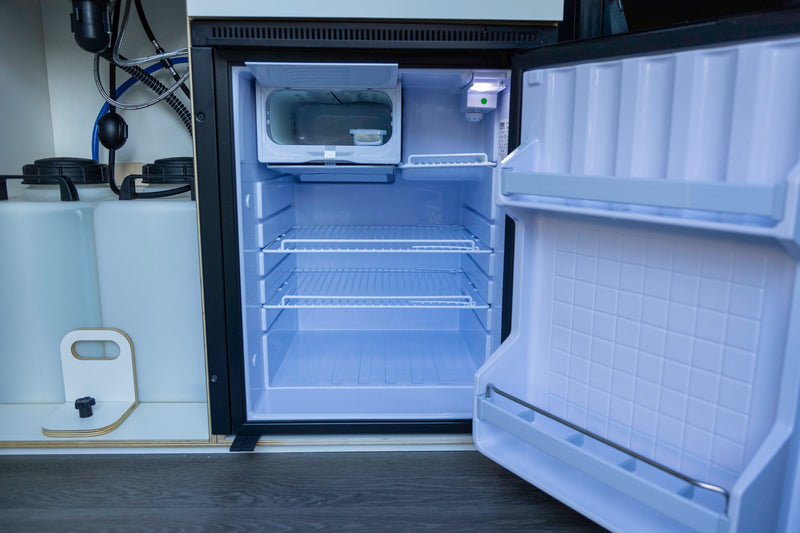 Compact RV rental kitchen features an open mini-fridge, water tanks, and plumbing, ready for adventure. — photo 20