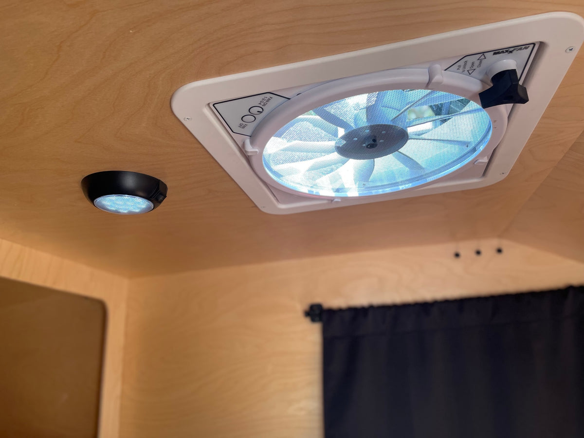 Interior of an RV rental showing a bright MaxxFan ceiling vent and LED light in a wood-paneled space. — photo 5