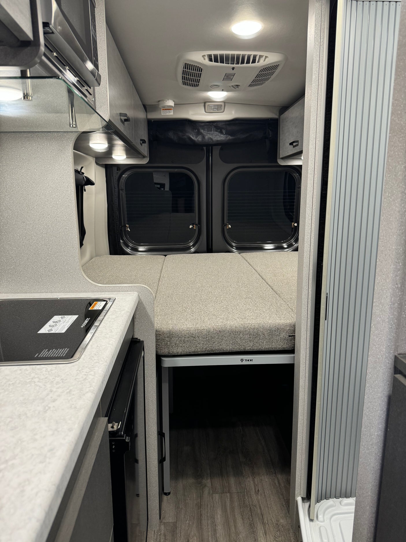 View inside an RV rental featuring a Dometic cooktop, Thor bed setup, and modern camper van interior details.