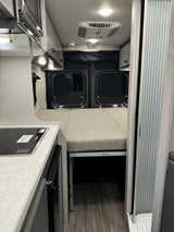 View inside an RV rental featuring a Dometic cooktop, Thor bed setup, and modern camper van interior details.
