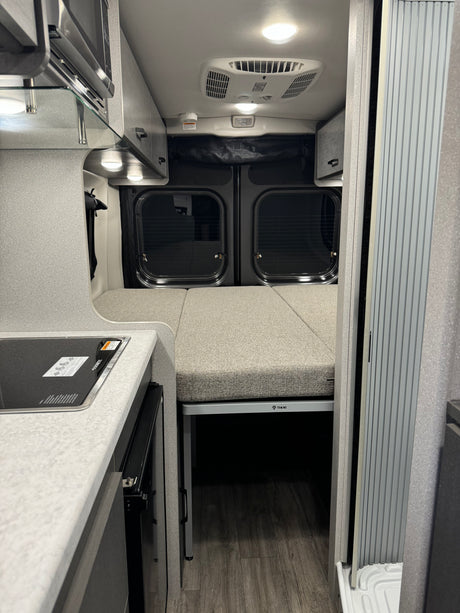 View inside an RV rental featuring a Dometic cooktop, Thor bed setup, and modern camper van interior details.