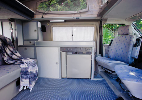 RV rental interior: pop-top camper with a compact kitchen, built-in fridge, patterned seats, and a cozy blanket.