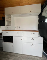 Interior of an RV rental: white modular kitchen cabinetry, built-in microwave, storage, power outlets, and wood ceiling.