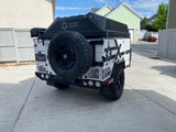 This white and black Patriot Campers off-road RV rental, equipped for adventure, is parked on a driveway.