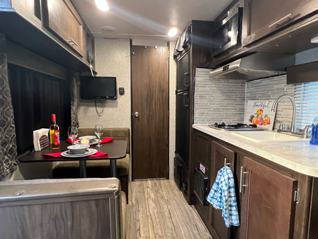Cozy RV rental interior featuring a compact kitchen, dining area with dinette seating, and mounted TV.