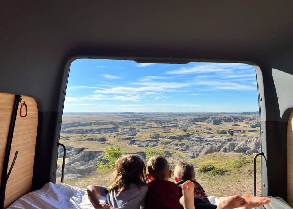  with a child enjoying the vast landscape.|A family poses with their RV rental at Devils Tower. Kids wave from the roof — photo 3