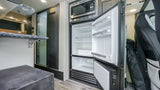 Compact rv rental interior with a kitchenette featuring an open refrigerator, microwave, and counter space.