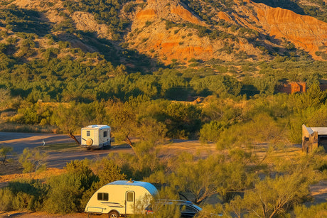 RV rental adventure in a stunning natural setting: two RVs camped amidst green foliage and vibrant red rock mountains.