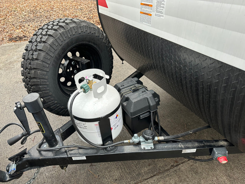Detail of an RV rental trailer's hitch area, featuring an off-road spare tire, propane tank, and battery. — photo 8