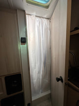 Inside an RV rental: a compact bathroom with a white shower curtain, overhead skylight, and Dometic thermostat.