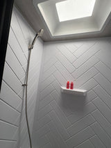 Modern and clean RV rental shower featuring stylish white herringbone walls, a skylight, and a handheld showerhead.