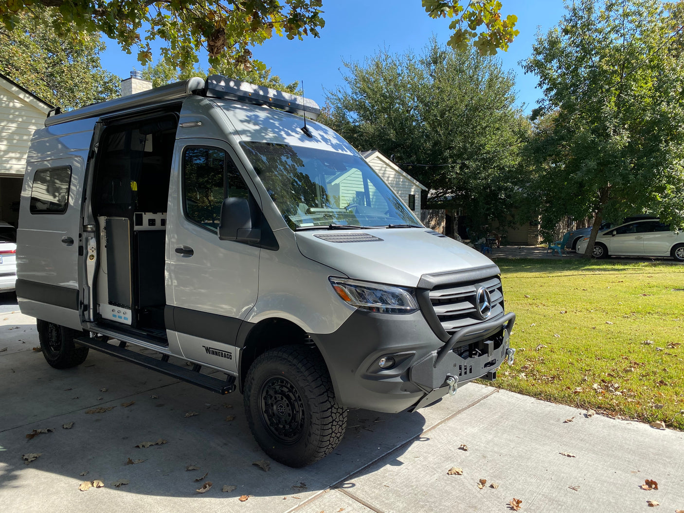 Custom Mercedes-Benz Sprinter Winnebago camper van with open side door, ideal for RV rental, parked on a driveway.