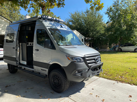 Custom Mercedes-Benz Sprinter Winnebago camper van with open side door, ideal for RV rental, parked on a driveway.